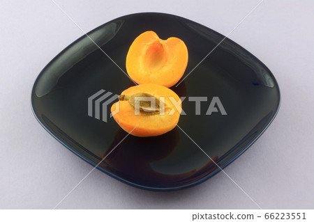 Fresh raw apricot halves with apricot pit on blue plate on lavender background Fresh raw apricot halves with apricot pit on blue plate on lavender background 66223551