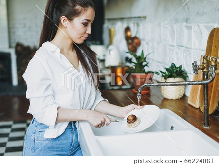 Young woman washes dishes with wooden brush Young woman washes dishes with wooden brush 66224081