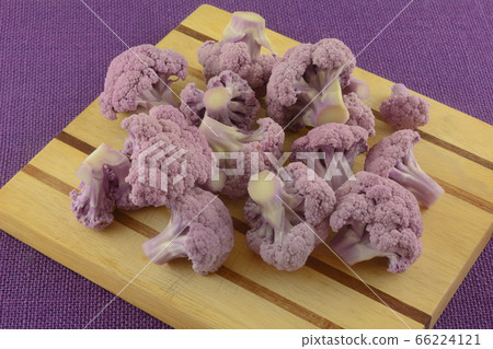 Purple cauliflower florets on wooden cutting board on purple tablecloth 66224121