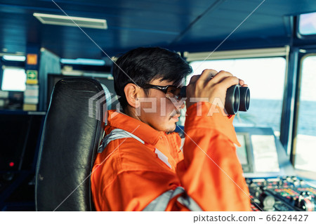 Filipino deck Officer on bridge of vessel or ship looking through binoculars Filipino deck Officer on bridge of vessel or ship looking through binoculars 66224427