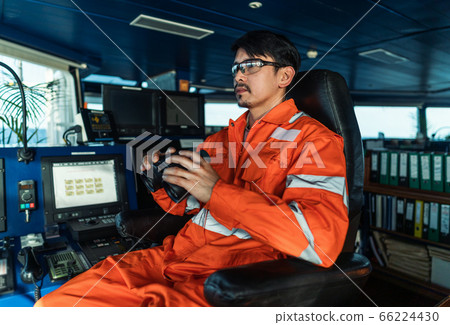 Filipino deck Officer on bridge of vessel or ship looking through binoculars 66224430