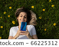 top view of young blonde woman lying on grass and using smartphone 66225312