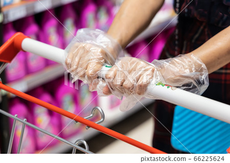 Close-up  of woman wearing disposable gloves pushing shopping cart shopping in supermarket 66225624