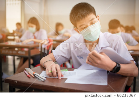 An Asian high school students in a white school uniform wearing a mask to do final exams in the midst of Coronavirus disease 2019 (COVID-19) epidemic and PM 2.5. An Asian high school students in a white school uniform wearing a mask to do final exams in the midst of Coronavirus disease 2019 (COVID-19) epidemic and PM 2.5. 66235367