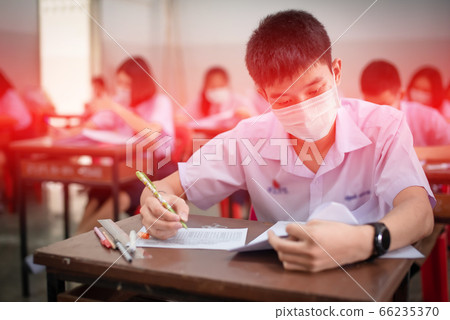 An Asian high school students in a white school uniform wearing a mask to do final exams in the midst of Coronavirus disease 2019 (COVID-19) epidemic and PM 2.5. 66235370