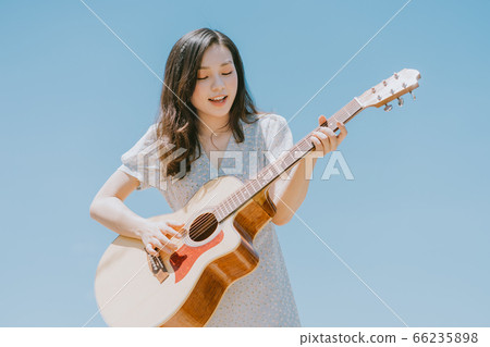 Beautiful woman playing guitar on blue sky background Beautiful woman playing guitar on blue sky background 66235898