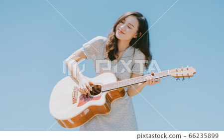 Beautiful woman playing guitar on blue sky background 66235899