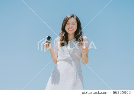Beautiful woman holding a camera on blue sky background Beautiful woman holding a camera on blue sky background 66235903