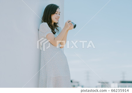A beautiful woman lean on the wall and holding a camera 66235914