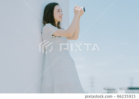 A beautiful woman lean on the wall and holding a camera A beautiful woman lean on the wall and holding a camera 66235915