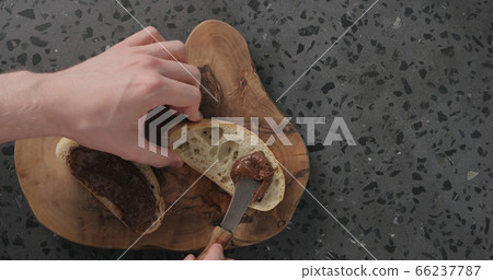 man spreading chocolate spread on ciabatta slice on olive board top view 66237787