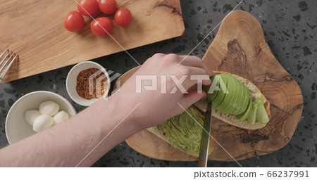 Top view man hands slice half of ripe avocado on ciabatta slice for making sandwich on concrete countertop Top view man hands slice half of ripe avocado on ciabatta slice for making sandwich on concrete countertop 66237991