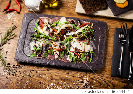 Beef carpaccio served on a board. Delicious healthy Italian traditional antipasti snacks closeup served for lunch with wine in modern gourmet restaurant. Beef carpaccio served on a board. Delicious healthy Italian traditional antipasti snacks closeup served for lunch with wine in modern gourmet restaurant. 66244465