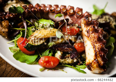 Warm octopus salad with stir fried vegetables and aji sauce on white plate. Delicious healthy mediterranean traditional seafood closeup served on a table for lunch. Warm octopus salad with stir fried vegetables and aji sauce on white plate. Delicious healthy mediterranean traditional seafood closeup served on a table for lunch. 66244482