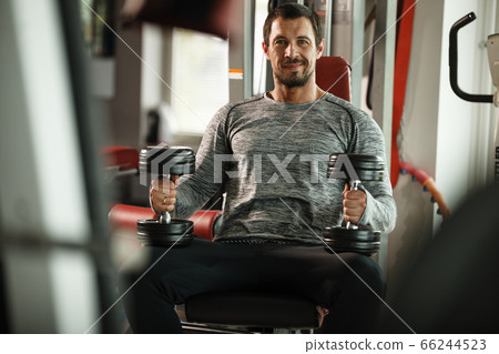 Fitness in gym, sport and healthy lifestyle concept. Handsome athletic man in grey shirt making exercises. Bodybuilder male model training biceps muscles with dumbbells Fitness in gym, sport and healthy lifestyle concept. Handsome athletic man in grey shirt making exercises. Bodybuilder male model training biceps muscles with dumbbells 66244523