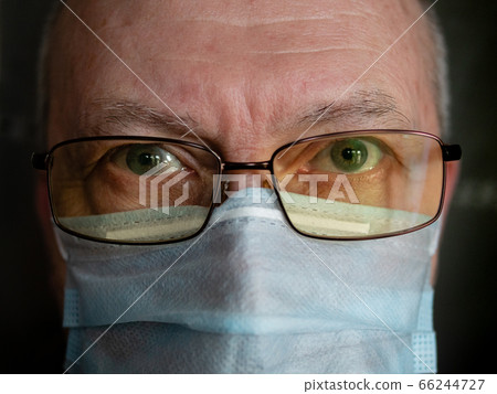 Close-up face portrait of senior man in medical mask and glasses looking at camera indoors 66244727