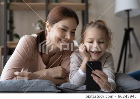 Smiling mom and little daughter watch video on cell together 66245943