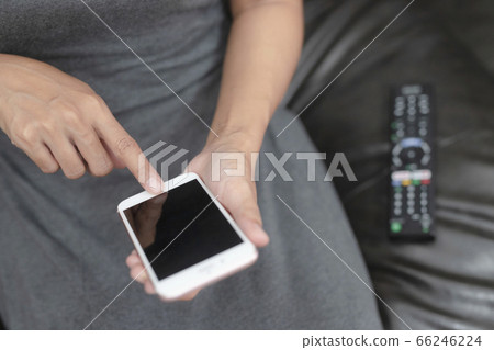 The hand is pressing the phone and remote control to select the channel by application in phone.Spend leisure time at home watching a movie. The hand is pressing the phone and remote control to select the channel by application in phone.Spend leisure time at home watching a movie. 66246224