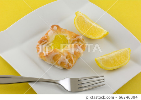 Mini lemon danish breakfast pastry with fresh lemon wedges on white plate with fork on yellow background Mini lemon danish breakfast pastry with fresh lemon wedges on white plate with fork on yellow background 66246394