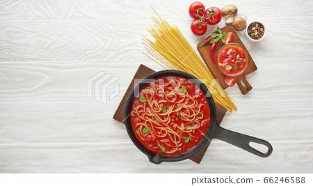 Cooking spaghetti with boiled tomato sauce in cast iron pan served with chili pepper, fresh basil, cherry-tomatoes and spices over white texture wooden background, ingredients food concept 66246588