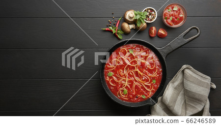 Homemade spaghetti with tomato sauce in cast iron pan served with red chili pepper, fresh basil, cherry-tomatoes and spices over black rustic wooden background, food cooking concept 66246589