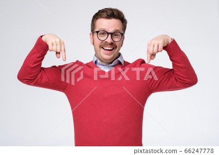 Attractive man in red sweater points down with both index fingers. Attractive man in red sweater points down with both index fingers. 66247778