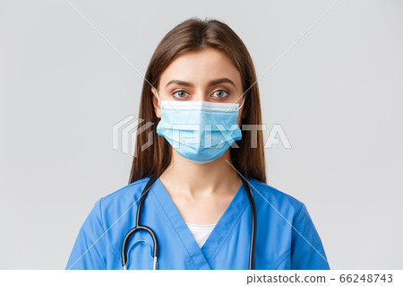 Covid-19, preventing virus, health, healthcare workers and quarantine concept. Close-up young female nurse or doctor in blue scrubs and medical mask looking serious at camera Covid-19, preventing virus, health, healthcare workers and quarantine concept. Close-up young female nurse or doctor in blue scrubs and medical mask looking serious at camera 66248743