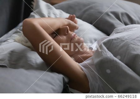Exhausted mature woman sleeping peacefully in home bed 66249118