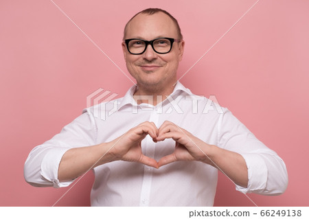 happy mature caucasian man in glasses showing heart symbol on pink background. happy mature caucasian man in glasses showing heart symbol on pink background. 66249138