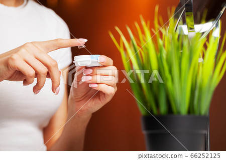 Woman removes contact lenses from a container with liquid 66252125