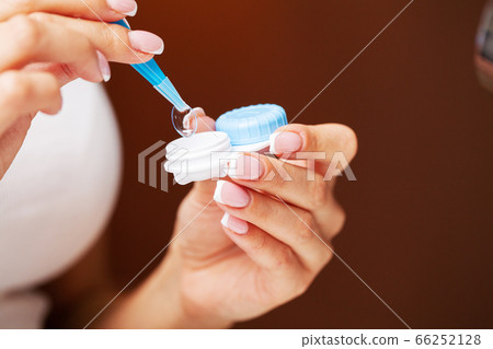 Woman removes contact lenses from a container with liquid 66252128