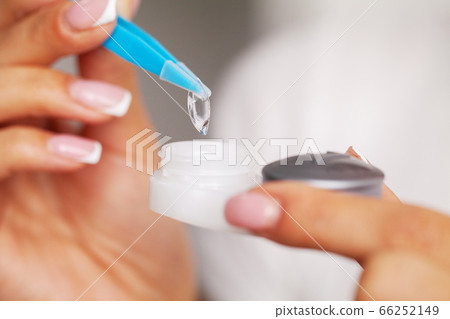 Woman removes contact lenses from a container with liquid 66252149