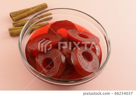 Red spiced apple rings in glass bowl with cinnamon sticks on pink background 66254037