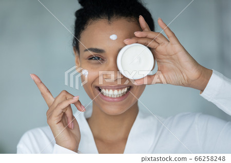 Head shot portrait satisfied African American woman demonstrating face cream 66258248