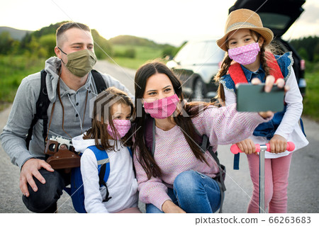 Family with two small daughters and face masks on trip outdoors in nature, taking selfie. Family with two small daughters and face masks on trip outdoors in nature, taking selfie. 66263683