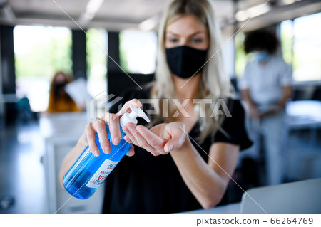 Young woman with face mask back at work in office after lockdown, disinfecting hands. 66264769