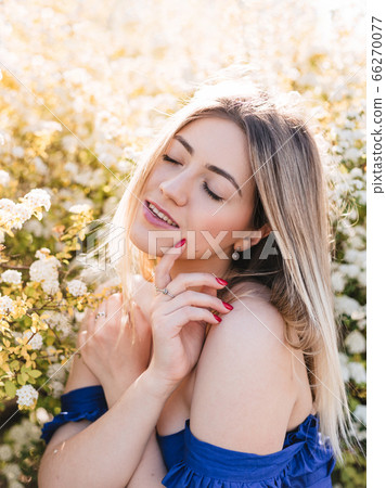 Sensual calm portrait of beautiful hipster woman in blooming bush with white flowers of spirea. Copy space. Stylish blonde woman in blue dress in garden 66270077