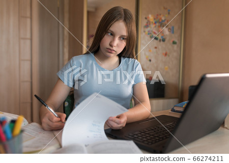 Teenager girl writing in notebooks and assignment notes, home education, preparation for college and school. Video conference on the Internet. Online communication with a teacher in a laptop. 66274211