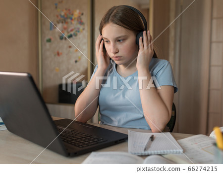teen girl, serious thoughtful, attentive concentrated, home lessons with laptop, video training on Internet. Watching in headphones, online communication. Preparing for difficult exam school college. 66274215