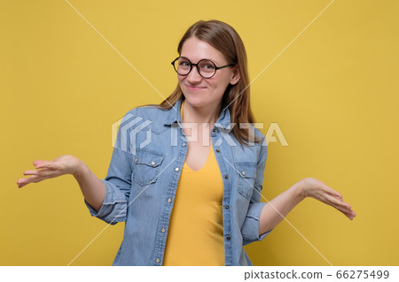 Smiling focused young woman with glasses, spreading hands, showing on both sides Smiling focused young woman with glasses, spreading hands, showing on both sides 66275499