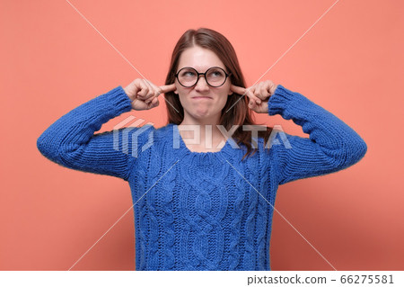 Young female in glasses having discontent look plugging her ears being annoyed with noise Young female in glasses having discontent look plugging her ears being annoyed with noise 66275581