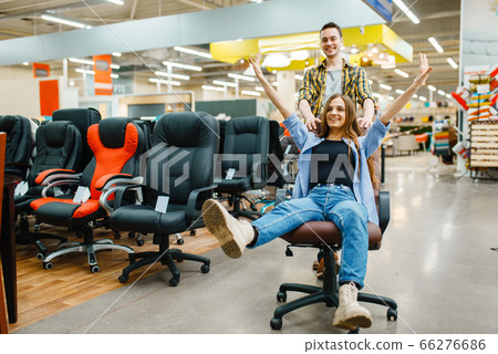 Couple rides on office chair in furniture store 66276686