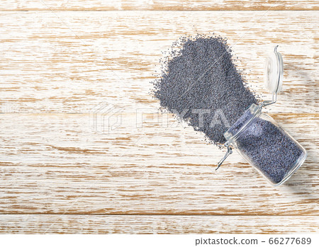 poppy seeds are poured from a glass jar on a white poppy seeds are poured from a glass jar on a white 66277689