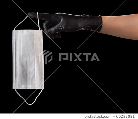 Hand in black gloves holding disposable face mask isolated on black background Hand in black gloves holding disposable face mask isolated on black background 66282081