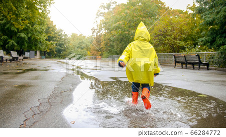 Little happy boy in rubber boots running over big puddle after rain at park Little happy boy in rubber boots running over big puddle after rain at park 66284772