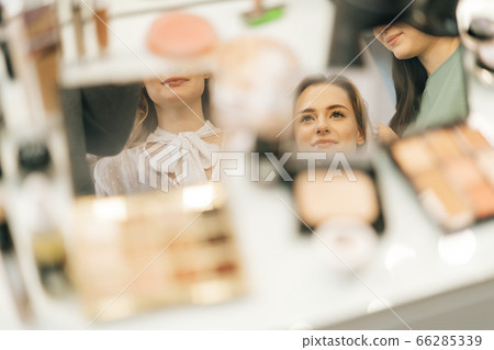 Close-up of faces of young woman and two female makeup artistes reflecting in mirror Close-up of faces of young woman and two female makeup artistes reflecting in mirror 66285339