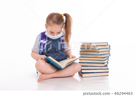 a first-grader learns to read. a little girl on home distance learning. A child in a medical mask reads a book. the student is doing homework. isolated on a white background 66294463