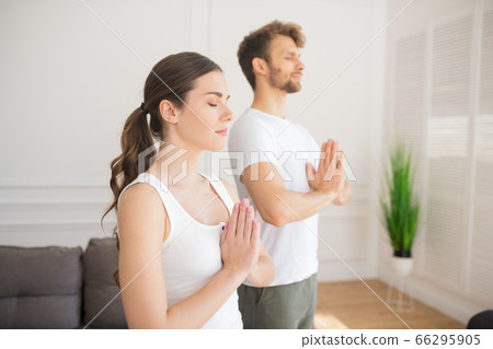 Young couple in white tshirts doing yoga at home putting their hands in namaste and feeling relaxed 66295905
