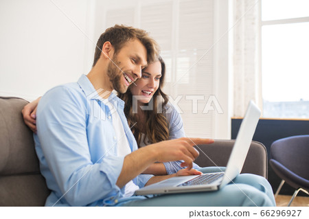 Young couple in denim sitting on a sofa watching something online Young couple in denim sitting on a sofa watching something online 66296927