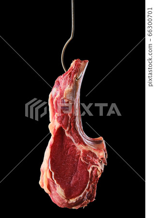 Beef ribeye steak bone-in on steel hook on black background 66300701